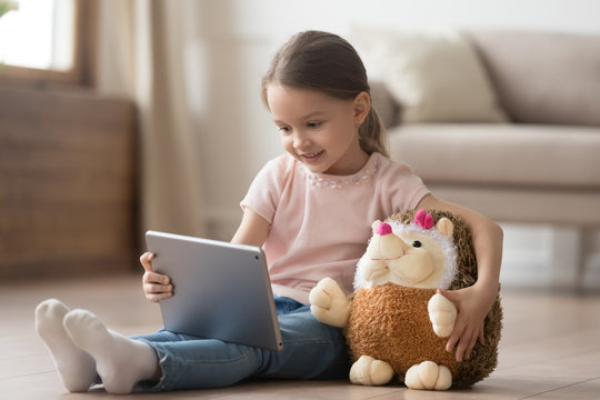 Curious child girl having fun using digital tablet embracing toy