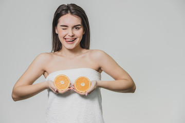 Happy young girl posing with fruits. Fragments of an orange in hands on a white background. Lifting the arms to the level of the chest, two pieces of fruit are kept.