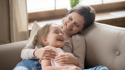 Happy mom embracing kid daughter laughing together lying on couch