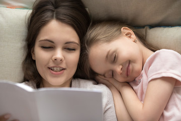 Happy little girl falling asleep in bed mum reading book