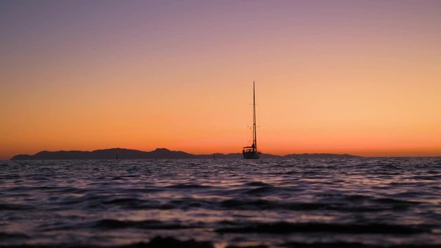 Zoom on sailboat silhouette anchored at sunset, shallow depth of field