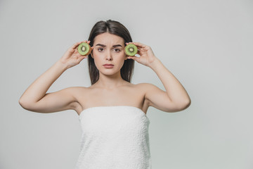 Young pretty girl standing on a white background. During this, at the level of the eye, the kiwi particles are kept in the hands.