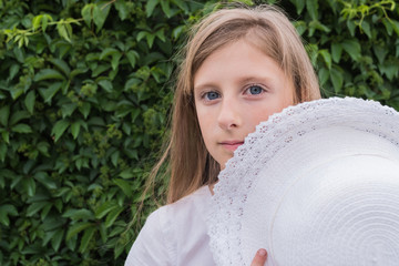 Portrait of a beautiful girl in a white dress and with a hat on a green grape leaf background