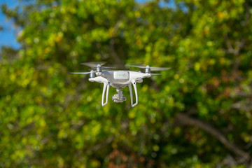 Drone in flight, green trees in the background, selective focus on the drone.