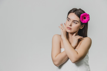 Beautiful young girl standing on a white background. During this time there is a flower in the hair. During this hand on the arm on the chest. Has beautiful black long hair.