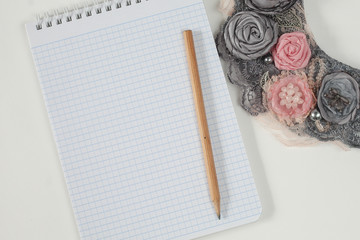 White notebook with a pencil on a gray table, a beautiful necklace of flowers. copyspace