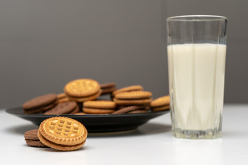 Chocolate and vanilla cookies and a glass of milk on white table on gray background