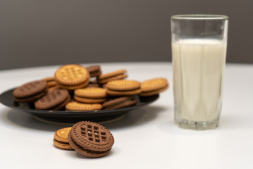 Chocolate and vanilla cookies and a glass of milk on white table