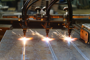 The machine cuts metal sheets with gas. Flying spray molten metal. Side view. three gas cutter...