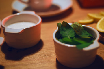 Peeled mint in a bowl, against the background of croissants, lemon and sugar on a wooden table.