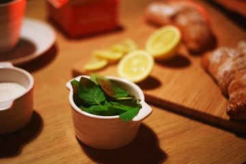Peeled mint in a bowl, against the background of croissants, lemon and sugar on a wooden table.