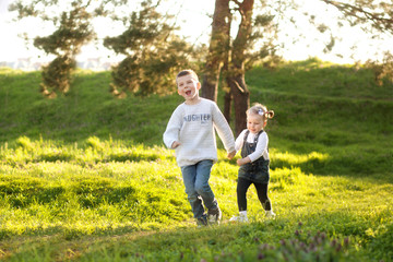 Fototapeta premium Cute children boy and girl friends running through the park in spring on a sunny day.