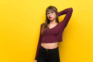 Woman with glasses over yellow wall having doubts