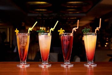 Row of different cocktails with straws on a dark background.