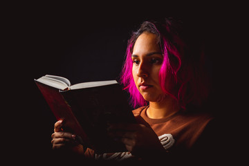 Portrait of young woman reading a book on black background low key