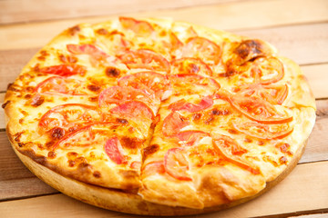 Pizza with tomatoes on a wooden tray on a wooden background. Top view