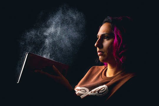 portrait of young woman slapping a dusty book on black background low key
