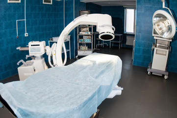 Modern operating room with X-ray medical scan, operating table, special lamp and medical devices.