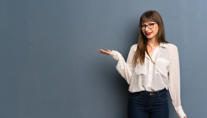 Woman with glasses over blue wall holding copyspace imaginary on the palm to insert an ad