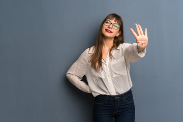 Woman with glasses over blue wall happy and counting four with fingers