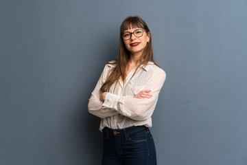Woman with glasses over blue wall with arms crossed and looking forward