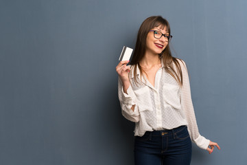 Fototapeta premium Woman with glasses over blue wall holding a credit card