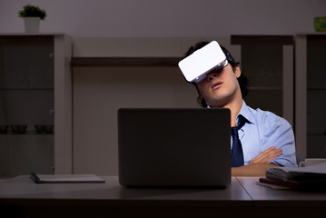 Young employee with virtual glasses at night in the office 