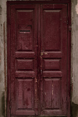 Old wooden door. Grunge wooden door painted maroon. Vintage house facade with a door. Wood vinous texture of a door. Old burgundy grunge texture. Vintage red wooden door.
