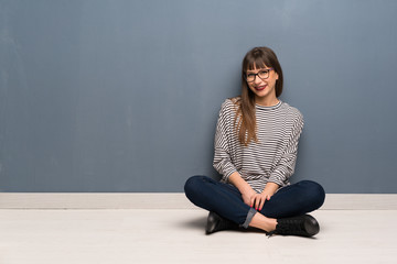 Woman with glasses sitting on the floor laughing looking to the front