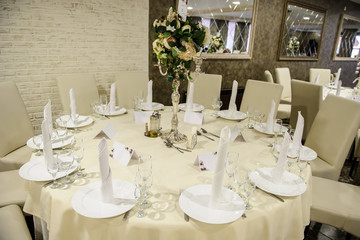 wedding table setting in a banquet hall in white color: a round table with flower arrangement on it surrounded by chairs