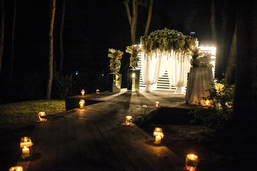 wedding arch decorated with flower compositions and curtains at night; a path with candles that goest to it