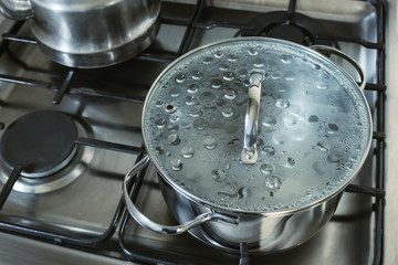 Stainless steel saucepan. Pot with a glass lid with boiling water is on the gas stove. Concept of cooking. Selective focus.