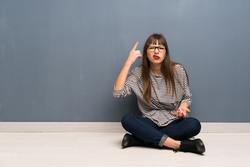 Woman with glasses sitting on the floor making the gesture of madness putting finger on the head