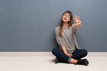 Woman with glasses sitting on the floor happy and counting three with fingers