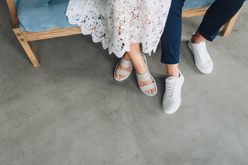 The guy and the girl are sitting on the couch in white shoes and sandals. Bride and groom in...