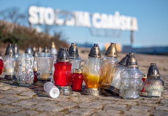 Candles, lanterns close up with Gdansk Shipyard gate in the background. (