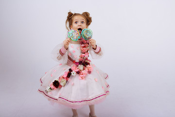 little girl in a pink dress with flowers holding a candy on a stick, licking, sweets in childhood. sweet life.