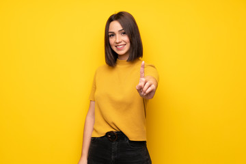Young woman over yellow wall showing and lifting a finger