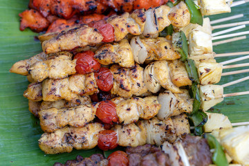 Skewers with pieces of grilled barbecue, green bell pepper, red tomato and meat for sell in street market, Thailand, closeup
