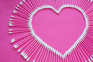 cotton buds laid out in the shape of a heart on a pink background