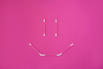 top view on pink cotton buds with white heads laid out in smile face form on a pink background