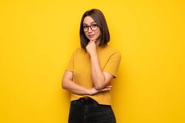 Young woman over yellow wall with glasses and smiling