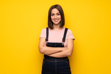 Young woman over yellow wall keeping the arms crossed in frontal position