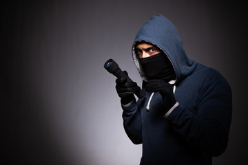 Young gangster in hood on grey background 