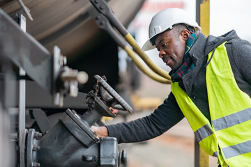 Afro-American train mechanic wearing safety equipment (helmet and jacket) checking and inspecting...
