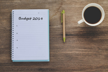 Budget 2019 Plan text on book note with cup of coffee, pen and smartphone.