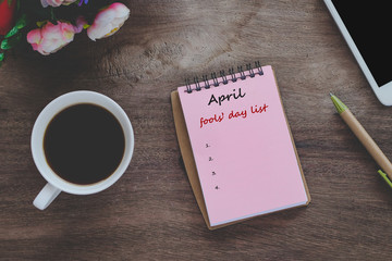 April fools' day text list on book note with cup of coffee, pen and smartphone.