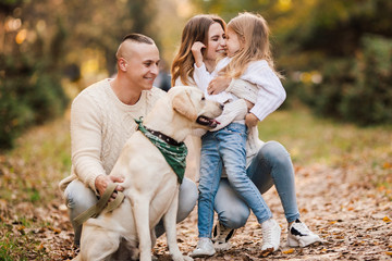 Fototapeta premium Szczęśliwa piękna rodzina z psem labradorem bawi się razem spacerując po parku.