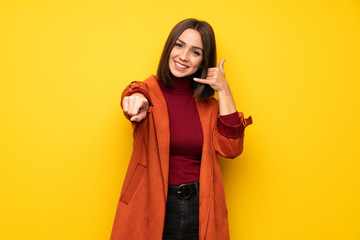 Young woman with coat making phone gesture and pointing front