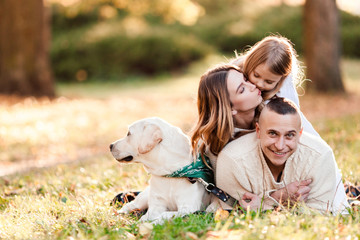 Fototapeta premium Happy family is having fun with dog labrador are lying on green grass in park.